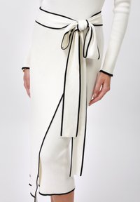 Knit white skirt with black accents, featuring a tied waist detail. The fabric has a ribbed texture and a side slit for added movement.