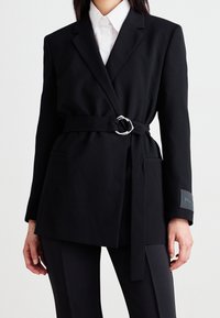 Sort blazer lavet af glat stof, med en indpakningsdesign, oversized pasform, lange ærmer og et bælte med sølvfarvet ring samt lommer.