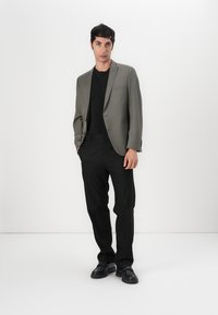 Blazer gris sobre una camiseta negra, combinado con pantalones negros y zapatos negros. Tejido suave, corte entallado y diseño minimalista.