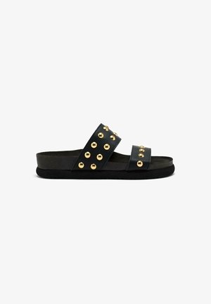 Chanclas negras con dos tiras anchas que presentan tachuelas doradas, suelas planas y una plantilla texturizada para mayor comodidad.