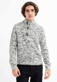 Suéter de punto en blanco y negro con un patrón texturizado y jaspeado. Presenta un cuello alto, tres botones y puños acanalados.