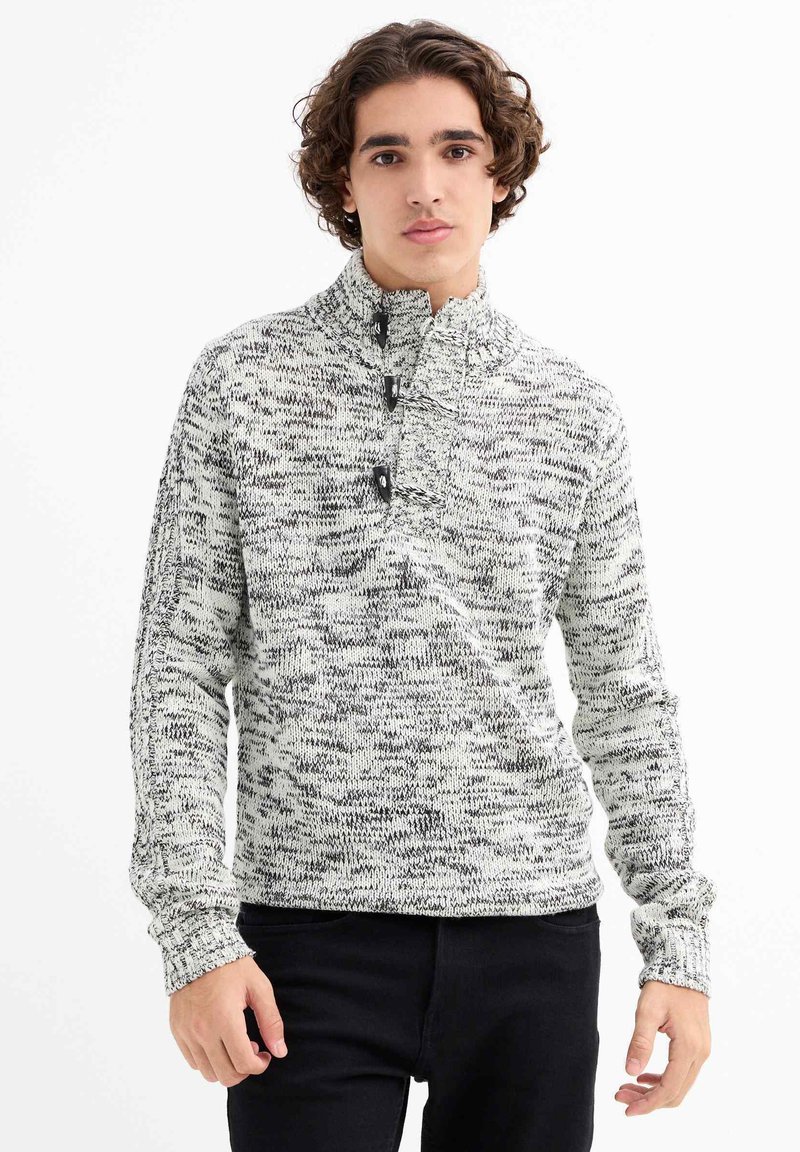 Suéter de punto en blanco y negro con un patrón texturizado y jaspeado. Presenta un cuello alto, tres botones y puños acanalados.