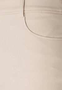 Tissu en mélange de coton beige avec une texture lisse, comportant une poche latérale et de subtils détails de couture le long de la taille.