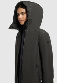 Tmavosivý zimný kabát s veľkou kapucňou, zipsom vpredu a bočnými vreckami; hladká, matná textúra s gombíkovými detailmi na golieri.