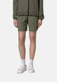 Shorts verdi realizzati in tessuto leggero, con un design semplice, taglio dritto e tasche. Abbinati a sneakers bianche e calzini.