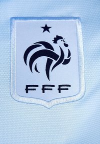 Un tissu tissé blanc et bleu clair présente un logo en forme de bouclier noir avec un coq et le texte "FFF" en bas. Une étoile au-dessus du logo.