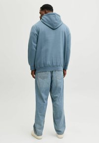 Sweat à capuche en tissu doux bleu poussiéreux avec ourlet et poignets côtelés, assorti à un jean en denim bleu clair et des chaussures blanches.