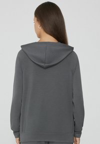 Sudadera con capucha gris hecha de tejido suave. Presenta un bolsillo tipo canguro y puños acanalados, con un corte relajado y un diseño sencillo.