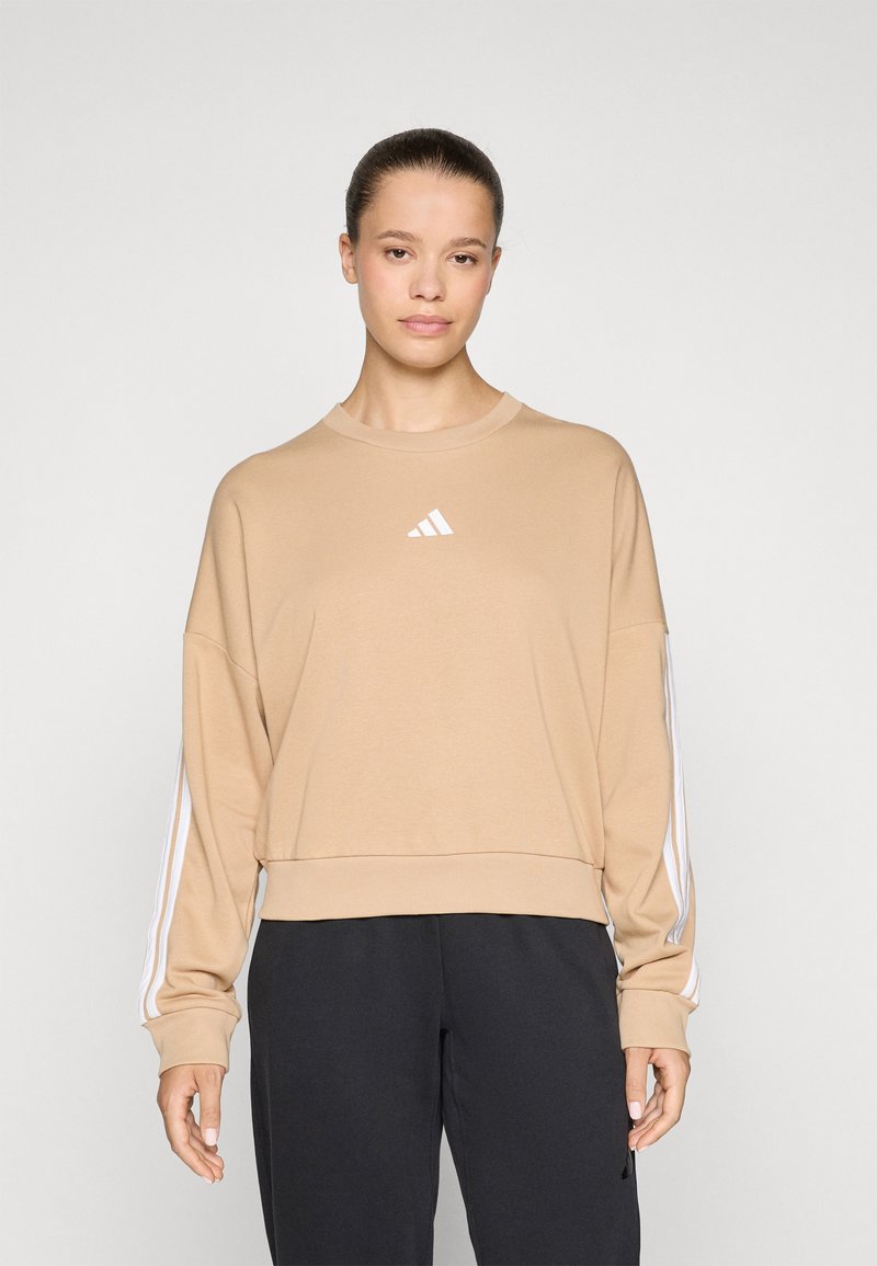 Beige hettegenser med rund hals og hvit Adidas-logo. Har hvite striper på lange ermer og en avslappet passform.
