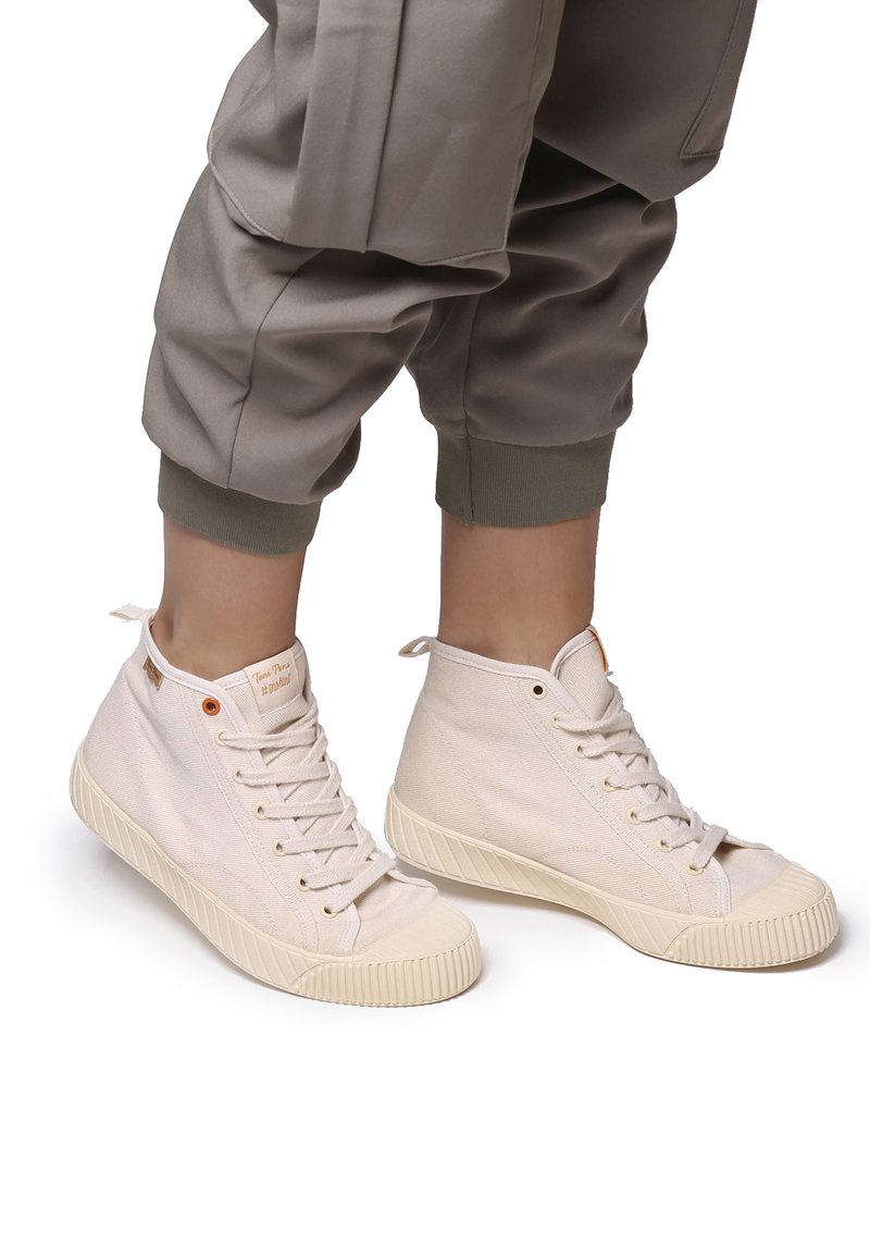 Zapatillas altas de lona en beige claro con suelas de goma texturizada, cordones planos y punteras reforzadas. Presenta un detalle de marca minimalista.