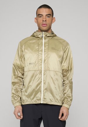 Let jakke i metallisk guld med hætte, lynlås foran, elastiske manchetter og sidelommer; har mærkning på brystet.