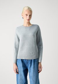 Vaaleanharmaa neulepaita, jossa on pyöreä kaulus ja ribbireunus, valmistettu pehmeästä materiaalista. Pitkät hihat ja hieman tekstuuripintainen viimeistely.