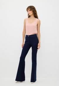 Ärmlös rosa topp i kombination med marinblå utsvängda byxor med en framknapp. Modellen står framför en enkel vit bakgrund.