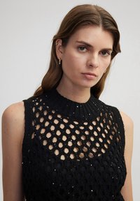 Top senza maniche nero con un design a maglia testurizzato, caratterizzato da fori a forma di diamante e sottili paillettes lungo il collo.