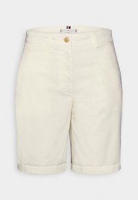 Short blanc longueur genou avec passants de ceinture, un bouton marron, poches avant et une petite étiquette de marque à l'intérieur de la ceinture.