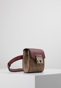 Mini håndtaske med en bordeaux tekstureret læderklap og en mønstrede brun krop. Har et guldlogo og lukkehardware.