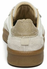 Sneaker bianco con accenti in suede beige, retro testurizzato e cuciture dettagliate sul tallone. Forma arrotondata e suola in gomma con leggera aderenza.