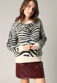 Pull à rayures noir et blanc en tricot doux, doté d'un col rond et de poignets côtelés, associé à une mini-jupe en cuir bordeaux brillant.