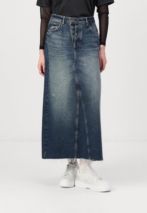 Denim maxi skirt in dark blue with a frayed hem, five-button closure, and front seam detail. Paired with white sneakers.