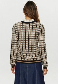 Strickpullover mit einem Karomuster in Creme, Braun und Schwarz, mit einem gerippten Saum und Bündchen. Die Rückansicht zeigt einen runden Halsausschnitt mit einer Rüschendekoration.