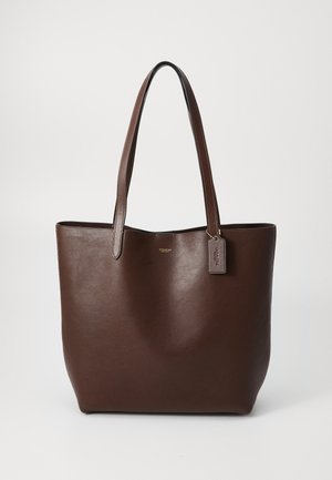 Borsa tote in pelle marrone scuro con due manici e un piccolo cartellino appeso su uno sfondo chiaro e uniforme.