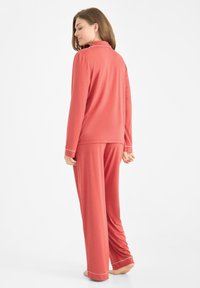 Roze pyjama set gemaakt van zachte stof. Langemouwen shirt met kraag en witte piping; bijpassende broek met vergelijkbare piping aan de zoom.