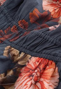 Material floral cu flori mari portocalii, roz și maronii pe un fundal întunecat de marină; cusături plisate de-a lungul liniei taliei.