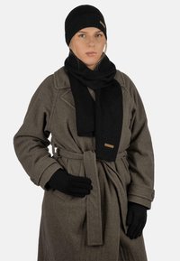 Schwarze gerippte Strickmütze, Schal und Handschuhe kombiniert mit einem grauen Wollmantel mit Gürtel und strukturiertem Stoff. Dezente braune Etikettendetail.