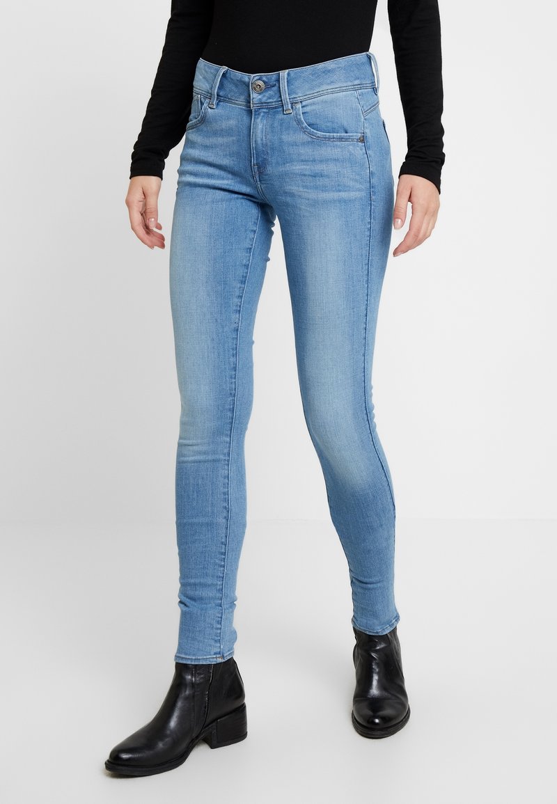 Jeans ajustados de color azul claro hechos de denim, que cuentan con un diseño clásico de cinco bolsillos, pasadores para cinturón y un cierre de botón simple en la cintura.