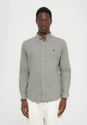 Chemise grise à boutons avec des manches longues et une texture douce. Présente un col classique et un petit logo brodé sur la poitrine.
