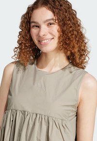 Lätthanterlig beige ärmlös topp med samlad volangkant, som har ett subtilt logotryck. Slät textur och avslappnad passform.