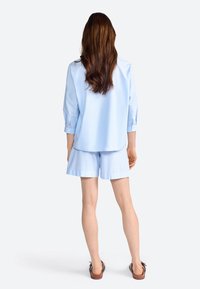 Chemise bleu clair à manches trois-quarts et shorts assortis. Matériau en coton avec une texture lisse et une coupe décontractée. Sandales marron.