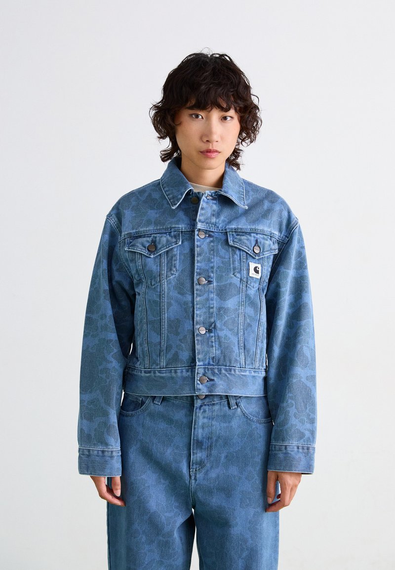 Veste en denim bleu au design court, présentant un motif subtil, deux poches poitrine et des boutons en métal argenté.