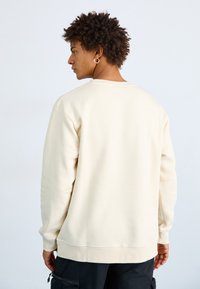 Sudadera crema de material suave, con escote redondo, puños y dobladillo acanalados. Diseño de espalda sin costuras y corte relajado.