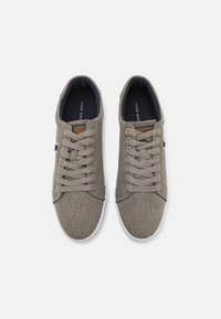 Gray canvas sneakers with a textured upper, white rubber sole, flat laces, and a brown leather accent on the tongue. Black insole lining.