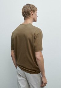 T-shirt marrone a maniche corte con colletto tondo, realizzato in morbido tessuto; presenta una vestibilità comoda e una texture liscia, mostrata da dietro.