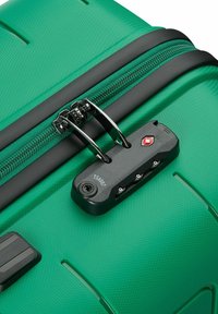 Maleta rígida verde con una superficie texturizada, cremallera negra y candado aprobado por la TSA que cuenta con tres diales de combinación para mayor seguridad.