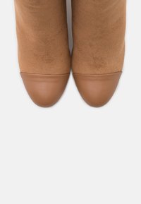 Bottines en daim marron avec un bout pointu en cuir lisse couleur beige. Texture douce avec des détails de coutures au niveau de la couture.