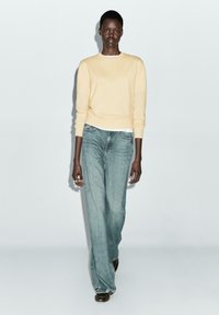 Yellow knit sweater and light blue wide-leg jeans. Sweater has ribbed cuffs and hem; jeans feature a classic five-pocket design and frayed hem.