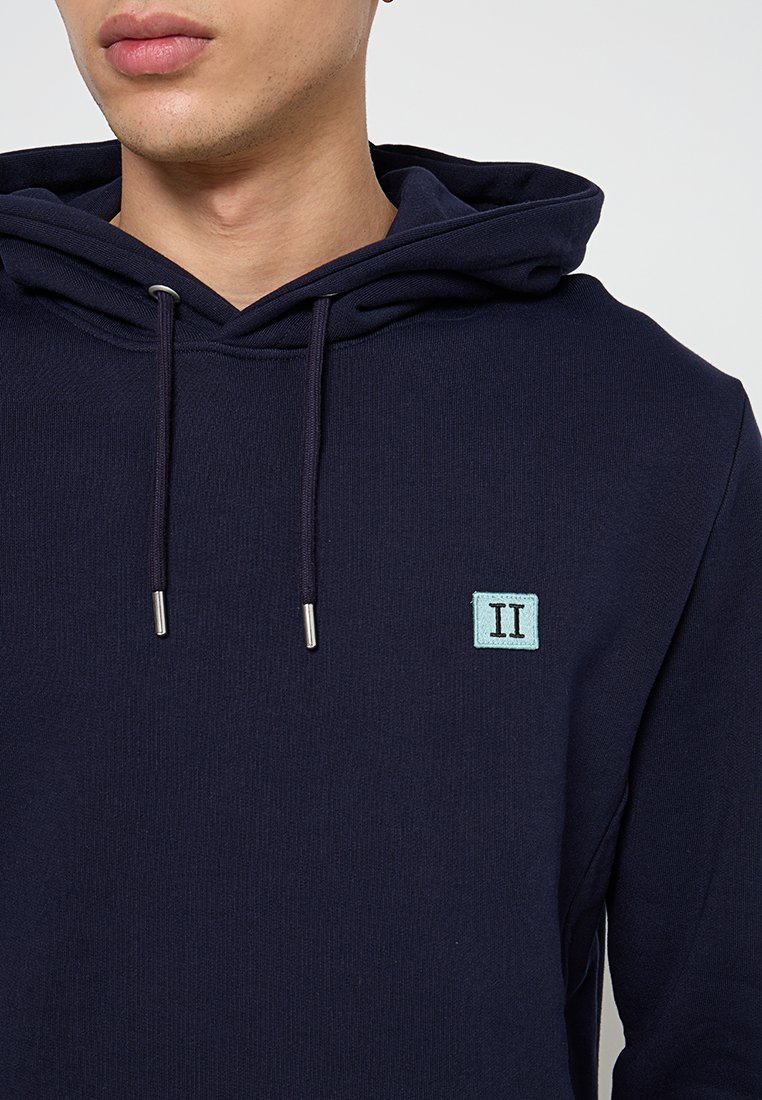 Felpa blu navy in tessuto testurizzato con occhielli e cordini argentati, caratterizzata da una toppa rettangolare blu chiaro con il logo 'II'.