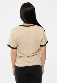 Beige t-shirt with dark brown ribbed collar and sleeve hems. Soft texture, relaxed fit, and no graphics or patterns visible on the back.
