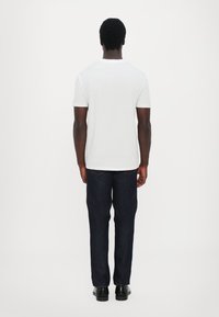 Hvit t-skjorte med korte ermer, glatt tekstur, rund halslinning, sammen med mørkeblå, rette jeans og svarte sko. Bakutsikt, minimalistisk design.