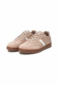 Zapatillas deportivas beige con una textura suave, que presentan rayas laterales blancas, punta redondeada y una suela de goma marrón.