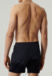 Nieprawdopodobnie wzorzyste bokserki w odcieniu granatowym z elastycznym paskiem w talii. Materiał wydaje się gładki. Model pokazany jest z tyłu, odsłaniając skórę oraz górną część ciała.