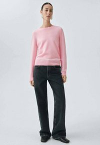 Suéter de punto rosa claro con un escote redondo, mangas largas y una textura suave, combinado con jeans oscuros de pierna ancha y botas negras.