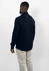 Donkerblauwe polo met lange mouwen en een kraag, gemaakt van zachte stof. Gekocht met lichtgekleurde, comfortabele broek. Eenvoudig en strak ontwerp.