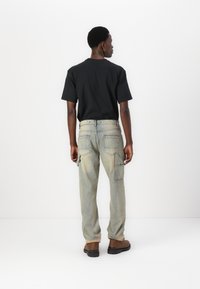Tricou negru cu mânecă scurtă, într-o croială lejeră, asociat cu pantaloni cargo decolorati, de un albastru deschis, care au multiple buzunare și un design drept al piciorului.