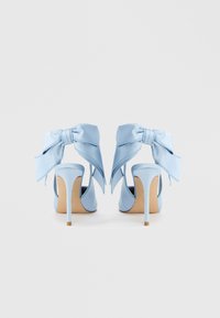 Γαλάζια ψηλοτάκουνα παπούτσια με σατινέ φινίρισμα, που διαθέτουν μεγάλα φιόγκους στον αστράγαλο και λεπτό τακούνι στιλέτο. Ομαλή υφή, ανοιχτή σχεδίαση πίσω.