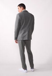 Grå skreddersydd dress med teksturert overflate, enkelt benspring bak, kombinert med hvite joggesko med blå detaljer.
