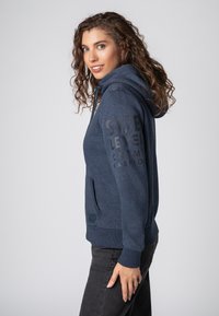 Marineblauwe katoenen hoodie met een kangoeroezak, ribgebreide manchetten en een trekkoord. Heeft bold, tonale tekst op de voorkant.